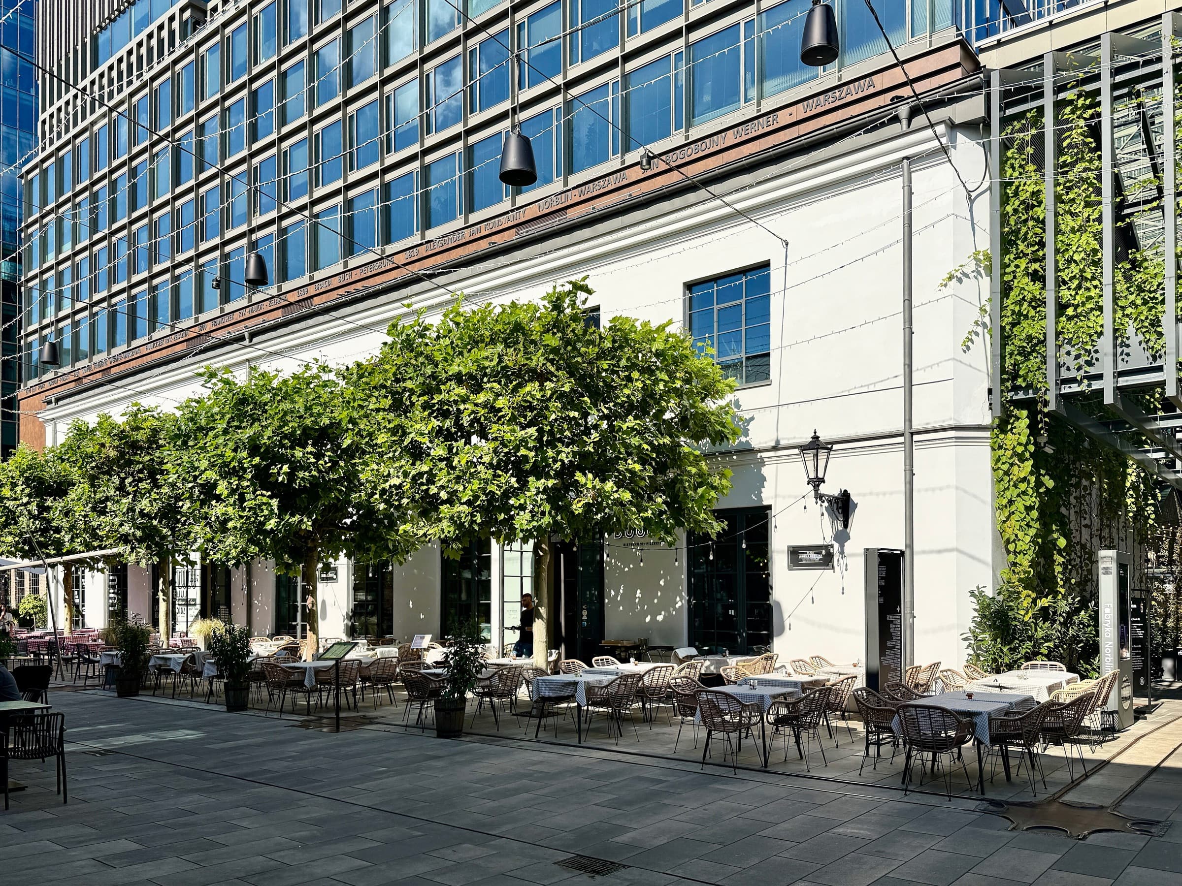 Restaurant terraces in front of a restored white factory building at Fabryka Norblina